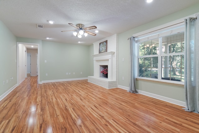 unfurnished living room featuring a fireplace, ceiling fan, light hardwood / wood-style floors, and a textured ceiling