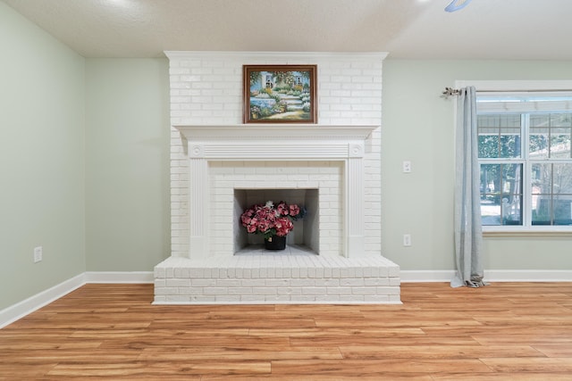 living room featuring a brick fireplace, a textured ceiling, and light hardwood / wood-style flooring