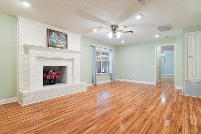 unfurnished living room featuring ceiling fan, a brick fireplace, light hardwood / wood-style floors, and a textured ceiling