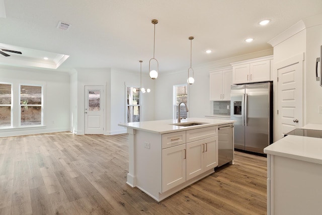 kitchen with pendant lighting, sink, stainless steel appliances, white cabinets, and a center island with sink