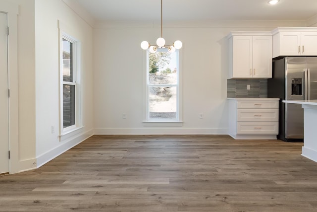 unfurnished dining area featuring an inviting chandelier, ornamental molding, and light hardwood / wood-style flooring