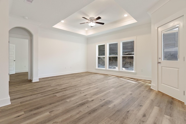 empty room with ceiling fan, ornamental molding, a tray ceiling, and light hardwood / wood-style flooring