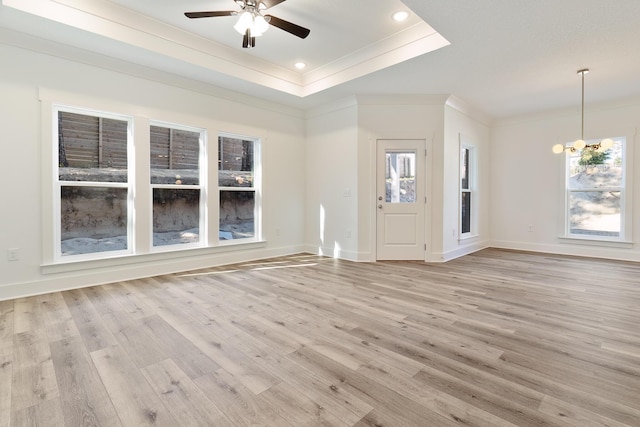 unfurnished living room featuring crown molding, ceiling fan with notable chandelier, light hardwood / wood-style floors, and a tray ceiling