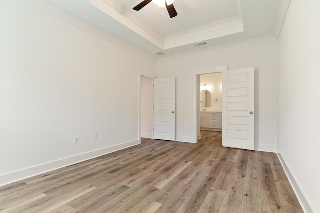 unfurnished bedroom featuring ceiling fan, connected bathroom, light hardwood / wood-style floors, ornamental molding, and a raised ceiling