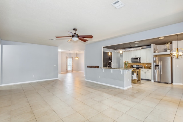 unfurnished living room featuring light tile patterned flooring and ceiling fan with notable chandelier