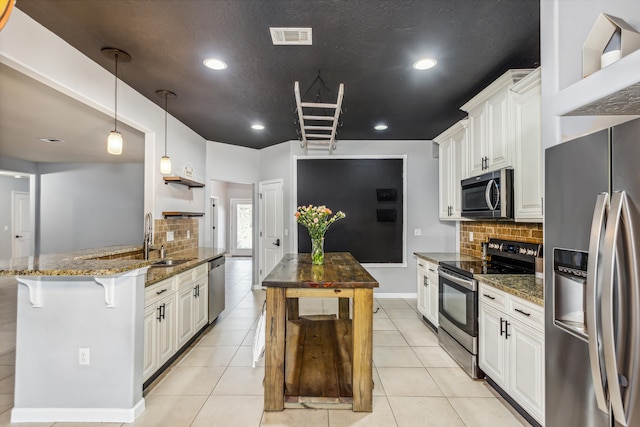 kitchen featuring stainless steel appliances, dark stone counters, a kitchen bar, pendant lighting, and white cabinets