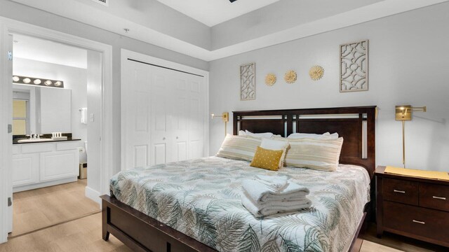 bedroom featuring a closet, ensuite bathroom, and light hardwood / wood-style flooring