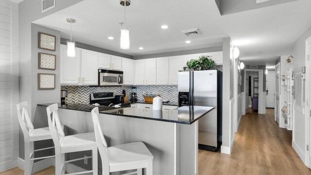 kitchen with decorative light fixtures, white cabinetry, appliances with stainless steel finishes, a breakfast bar area, and light wood-type flooring