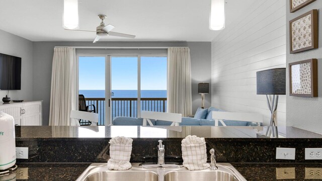 kitchen featuring a water view, wooden walls, sink, and ceiling fan