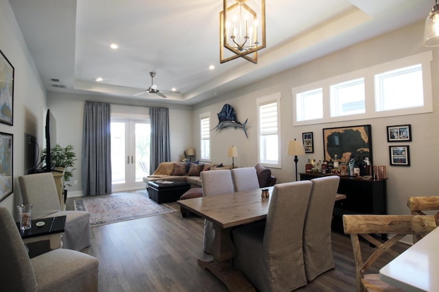 dining area featuring ceiling fan with notable chandelier, a raised ceiling, and dark hardwood / wood-style flooring