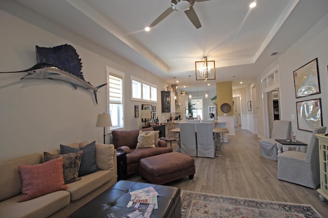 living room featuring ceiling fan with notable chandelier, a tray ceiling, and hardwood / wood-style flooring