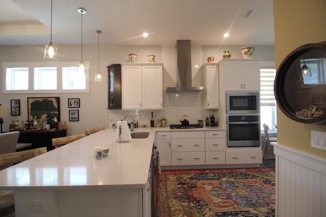 kitchen featuring wall chimney range hood, stainless steel appliances, and white cabinets