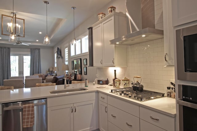 kitchen featuring white cabinetry, wall chimney exhaust hood, stainless steel appliances, decorative light fixtures, and sink