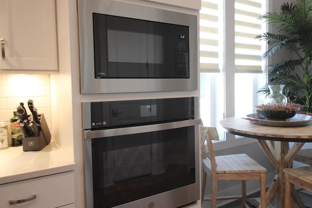 room details featuring decorative backsplash, white cabinets, built in microwave, and stainless steel oven