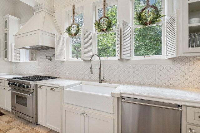 kitchen with white cabinets, sink, backsplash, stainless steel appliances, and custom range hood