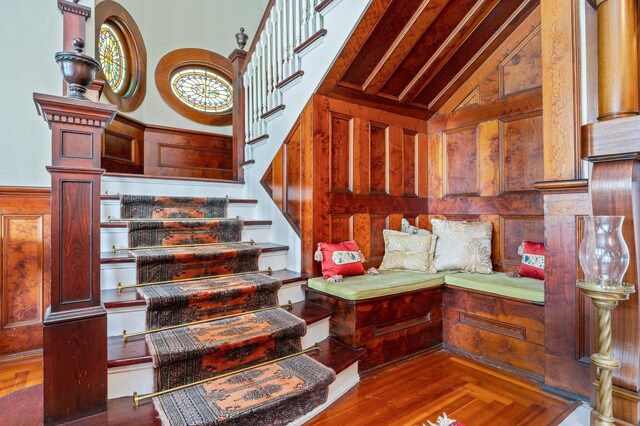 stairs featuring wood-type flooring, wooden walls, and high vaulted ceiling