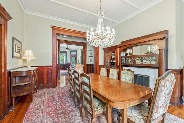 dining area with wood walls, wood-type flooring, ceiling fan with notable chandelier, coffered ceiling, and a fireplace