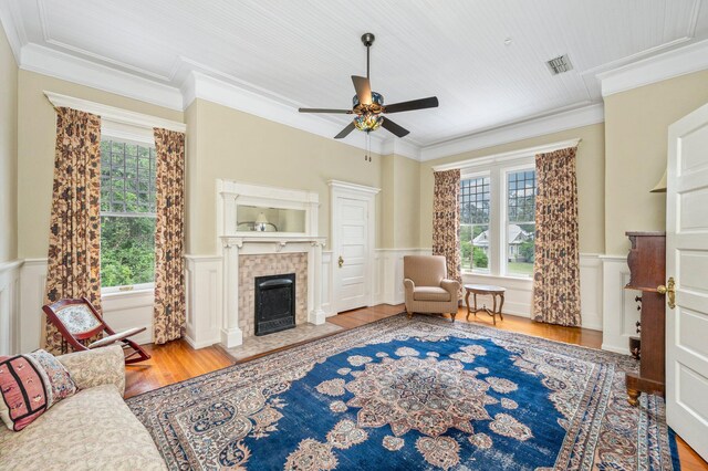 living room featuring a tiled fireplace, ceiling fan, wood-type flooring, and crown molding