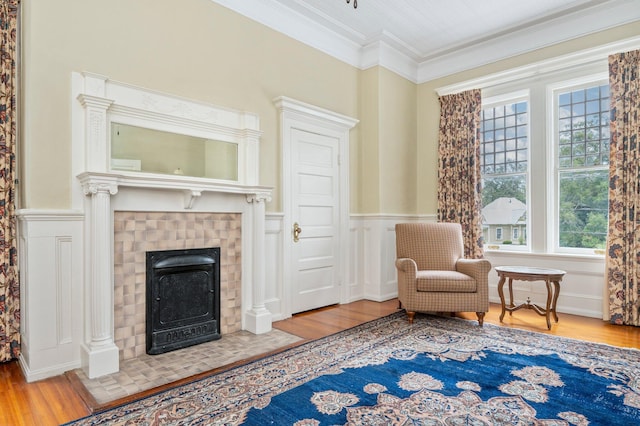 living area with wood-type flooring, a tiled fireplace, and crown molding