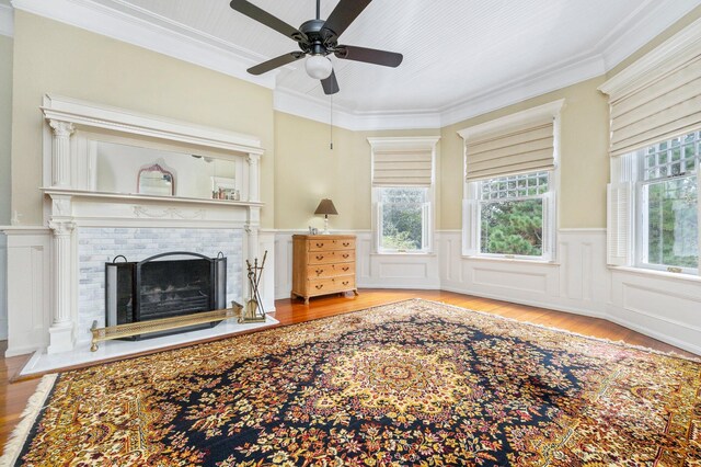 living room with a brick fireplace, crown molding, ceiling fan, and light wood-type flooring