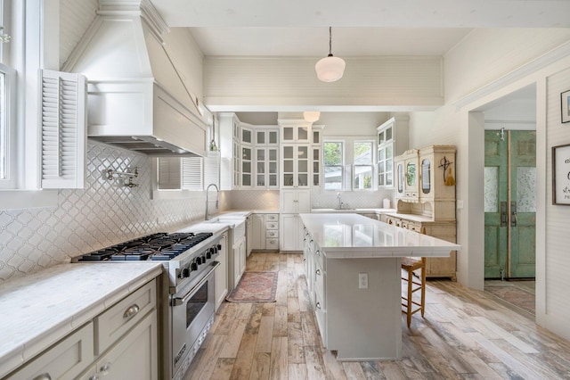 kitchen with stainless steel stove, pendant lighting, light hardwood / wood-style flooring, and decorative backsplash