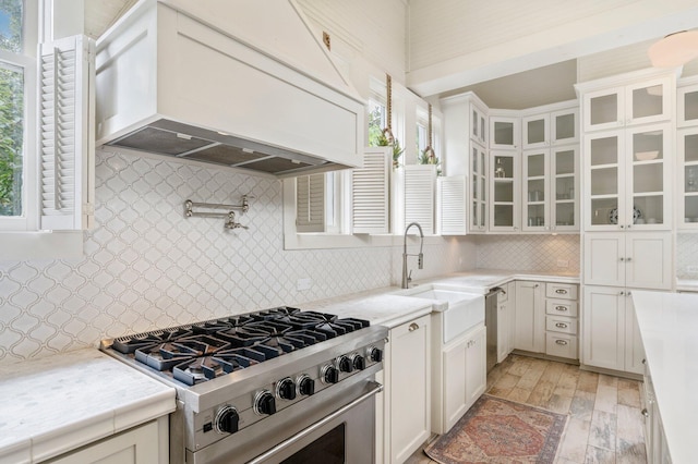 kitchen featuring custom exhaust hood, tasteful backsplash, white cabinetry, stainless steel appliances, and light wood-type flooring