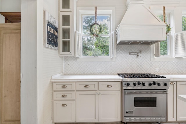 kitchen featuring custom range hood, designer stove, white cabinets, and decorative backsplash