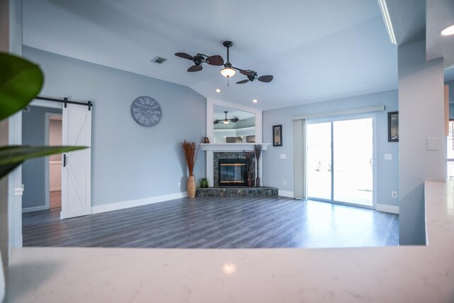 unfurnished living room with ceiling fan, a premium fireplace, dark wood-type flooring, a barn door, and vaulted ceiling