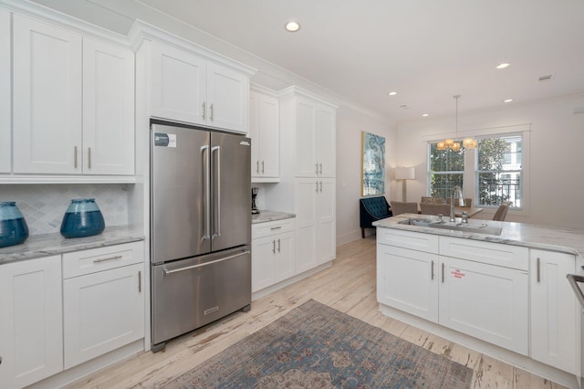 kitchen with sink, decorative backsplash, stainless steel fridge, a notable chandelier, and white cabinetry