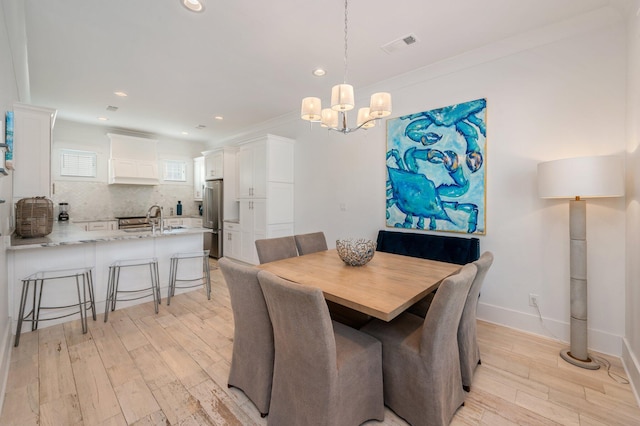 dining room featuring crown molding, light hardwood / wood-style flooring, a chandelier, and sink