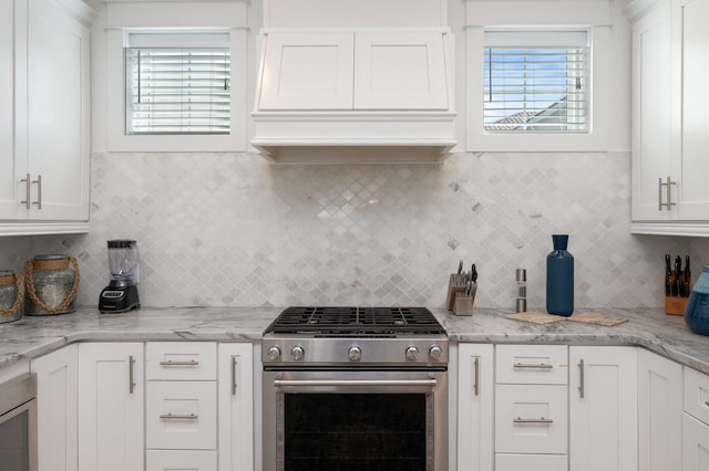 kitchen with light stone counters, white cabinetry, high end stainless steel range oven, and tasteful backsplash