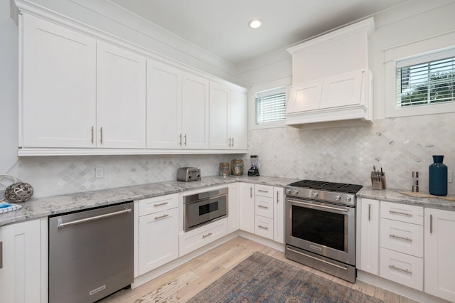 kitchen with premium range hood, white cabinets, light hardwood / wood-style flooring, light stone counters, and stainless steel appliances