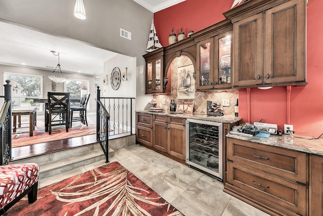 bar with hanging light fixtures, ornamental molding, beverage cooler, backsplash, and light stone countertops