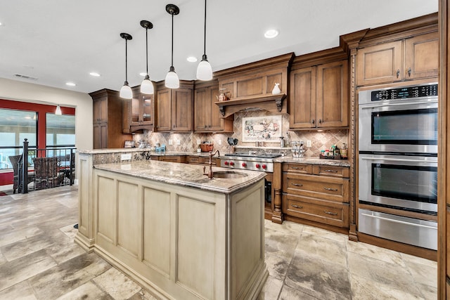 kitchen with an island with sink, sink, decorative light fixtures, appliances with stainless steel finishes, and light stone countertops