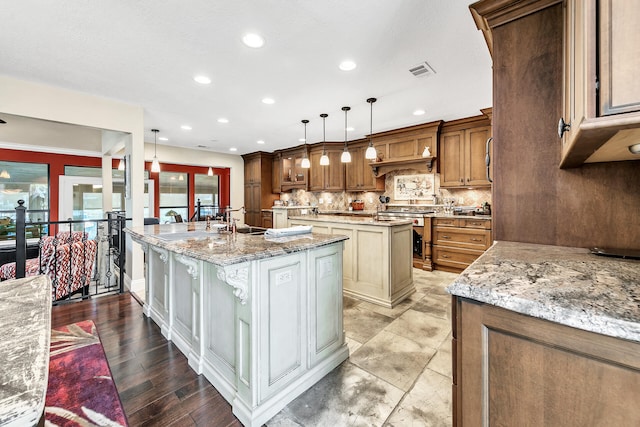 kitchen featuring light stone countertops, an island with sink, hanging light fixtures, tasteful backsplash, and light wood-type flooring