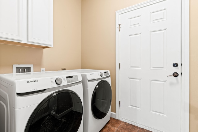 clothes washing area with washer and dryer, dark tile patterned flooring, and cabinets