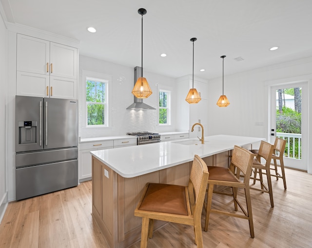 kitchen with sink, wall chimney exhaust hood, white cabinetry, stainless steel appliances, and a spacious island