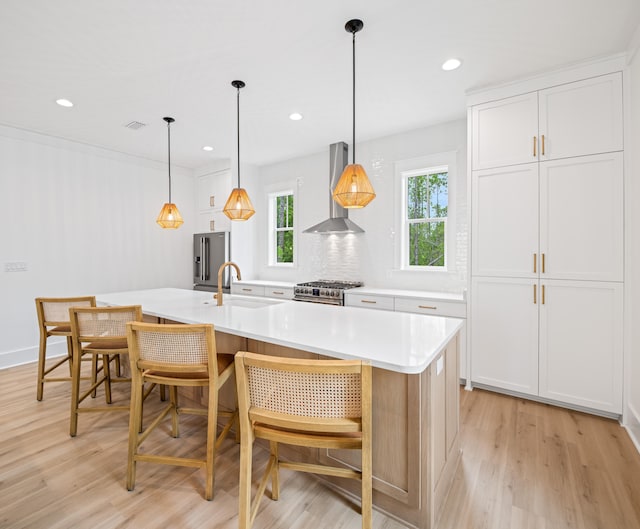 kitchen featuring a kitchen island with sink, sink, white cabinetry, wall chimney exhaust hood, and light hardwood / wood-style flooring