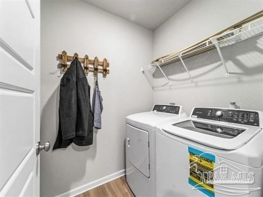 clothes washing area featuring laundry area, baseboards, washing machine and clothes dryer, and wood finished floors