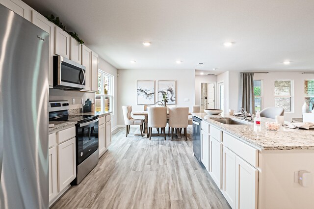 kitchen featuring light wood finished floors, appliances with stainless steel finishes, a kitchen island with sink, white cabinetry, and a sink