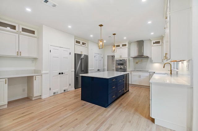 kitchen featuring light hardwood / wood-style flooring, stainless steel appliances, a kitchen island, and wall chimney range hood