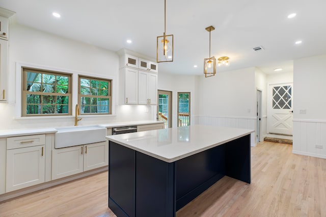 kitchen featuring sink, white cabinets, hanging light fixtures, a kitchen island, and light hardwood / wood-style flooring