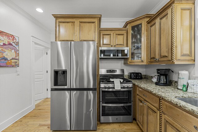 kitchen featuring ornamental molding, brown cabinets, light stone countertops, stainless steel appliances, and light wood-style floors