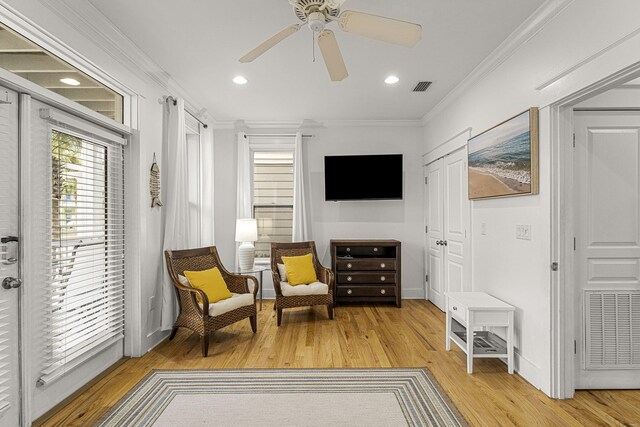 living area with light wood finished floors, visible vents, and crown molding