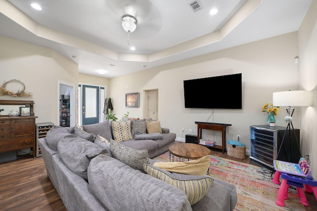 living room featuring ceiling fan, a raised ceiling, and dark hardwood / wood-style flooring