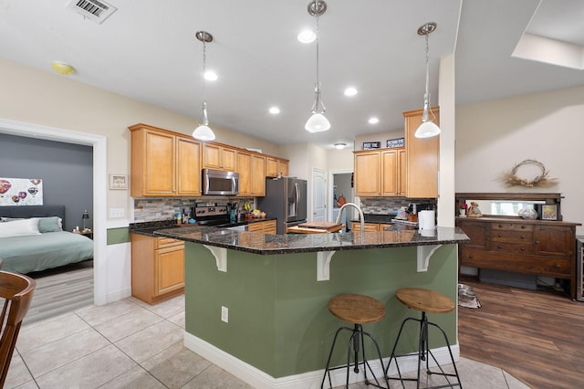 kitchen with dark stone counters, decorative backsplash, appliances with stainless steel finishes, and a kitchen bar