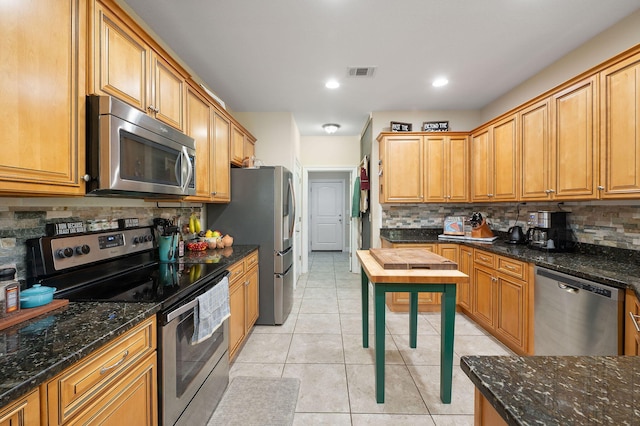 kitchen with dark stone counters, stainless steel appliances, backsplash, and light tile patterned floors