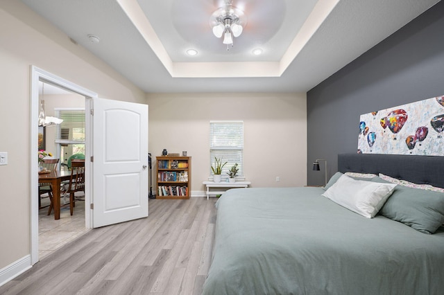 bedroom featuring light wood-type flooring, ceiling fan, and a raised ceiling