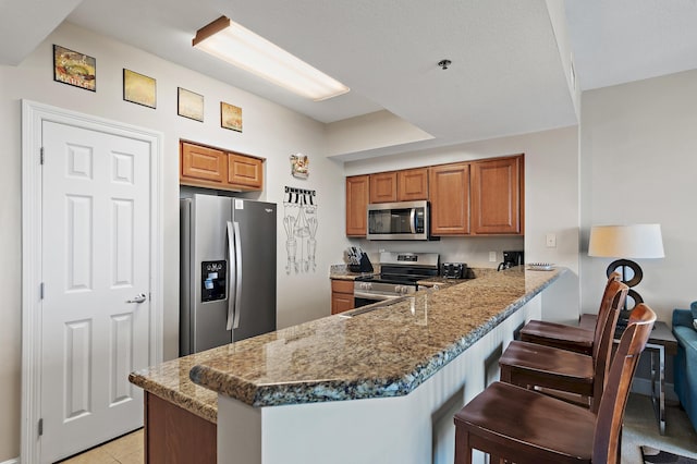 kitchen with dark stone countertops, stainless steel appliances, kitchen peninsula, and a kitchen breakfast bar