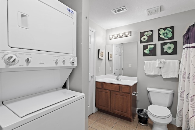 bathroom with vanity, tile patterned flooring, a textured ceiling, stacked washer and dryer, and toilet